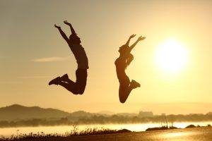 Fitness couple jumping happy at sunset with the sun in the background